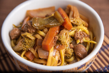 Vegan food, Vegan Yakisoba, with chopsticks in a bowl on bamboo mat, over wood, selective focus.