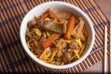 Vegan food, Vegan Yakisoba, with chopsticks in a bowl on bamboo mat, over wood, top view.
