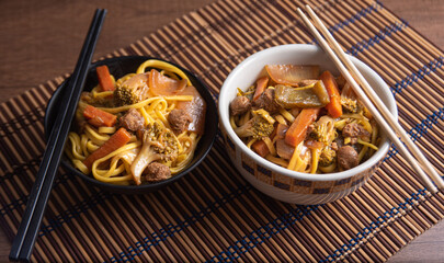 Vegan food, Vegan Yakisoba, with chopsticks in a bowl on bamboo mat, over wood, selective focus.