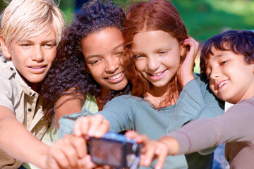Fototapeta premium Capturing childhsummer moments. A group of kids looking at a digital camera while sitting outside.