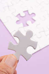 Hand holding Puzzle pieces Vertical on rose surface. White jigsaw game texture. Matching, inserting last missing part. Business and teamwork problem solving background. Copy space for text, close up.