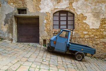 Stereotype scene on the streets of Volterra with a parked Piaggio Ape in front of an old rural...