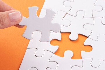 Fototapeta premium Hand holding Puzzle pieces on orange surface. White jigsaw game texture. Matching, inserting last missing part. Business and teamwork problem solving background. Copy space for add text, close up.
