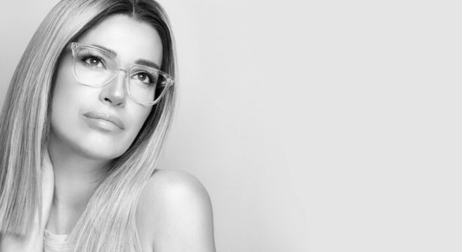 Monochrome beautiful woman wearing trendy nude glasses or eyewear looking up pensive in a panorama banner with copyspace