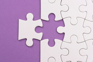 Puzzle pieces on lilac surface. White jigsaw game grid texture. Matching, inserting last missing part. Business and teamwork problem solving background. Copy space for add text, close up.