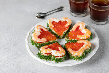 Canape in the form of hearts with red caviar and shrimp on a white plate on a light gray background, Valentine's Day breakfast idea