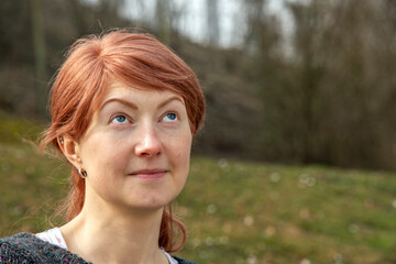 Young red-haired woman in the park looking upward