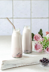 Milkshake from fresh blueberries and natural yogurt in bottles, beautiful serving on a light tray, a bouquet of roses on the table for decoration and creating a good mood, breakfast