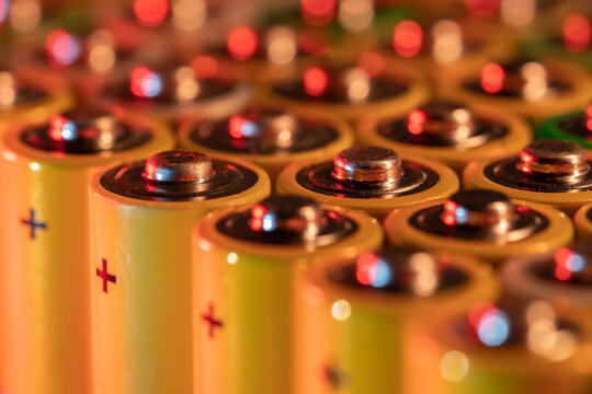 Closeup of positive ends of discharged batteries AA sizes, macro shot, selective focus. Used alkaline battery. Hazardous garbage concept. Neon yellow light