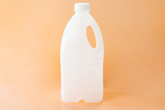 A big white gallon of milk without a label stands on the orange background. Advertising. Design. Shop. Single. One. Grocery. Pure. Person. Vitamin. Lid. Nutrient. Blank. Diet