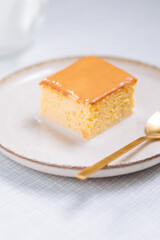 Dessert Called Tres Leches, traditional Albanian dessert made from biscuit, milk and caramel sauce. Served on bright background with golden spoon