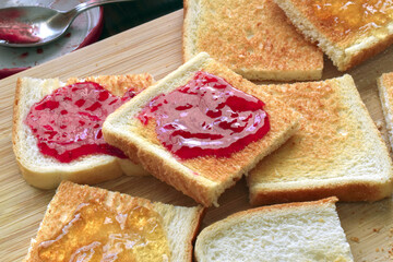 Toast with raspberry and orange jam a bamboo cutting board.  Spreading jam on bread.	