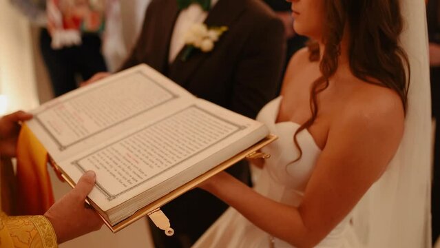 Khmelnytskyi, Ukraine - 09.19.2020: Newlyweds bride and groom get married. holy father priest in church holds bible book in his hands, reads prayer, turns pages. worship, divine service church, chapel