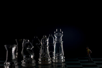 Miniature figure people as businessman standing face to face with King chess piece on chessboard. macro