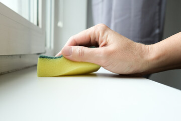Woman hand wiping dust from a window sill with a sponge, cleaning and tiding up the house every day