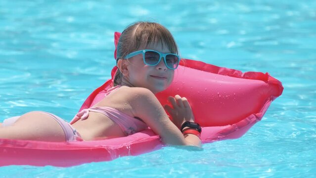 Young joyful child girl having fun swimming on inflatable air mattress in swimming pool with blue water on warm summer day on tropical vacations. Summertime activities concept