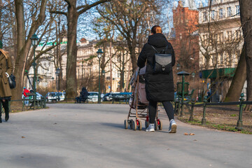 Close-up of a young mother in a black coat with a backpack on her back, walking from a baby...