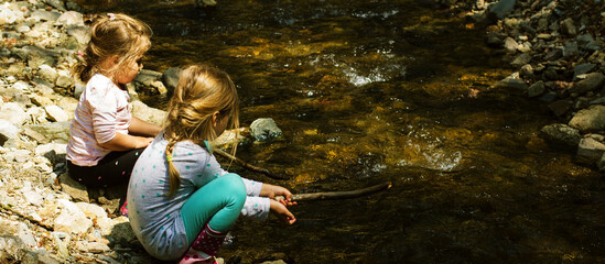 Two little girl playing by forest stream on spring day. Childhood in nature.