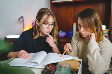 two women young caucasian female student sitting at home with her mentor teacher looking to the notebook explaining lesson study preparing for exam learning education concept real people copy space