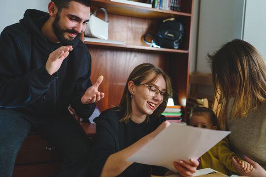 Group of people young woman caucasian female student sitting at home with her friends and family holding envelope with mail letter happy exited smiling reading entry test results success concept