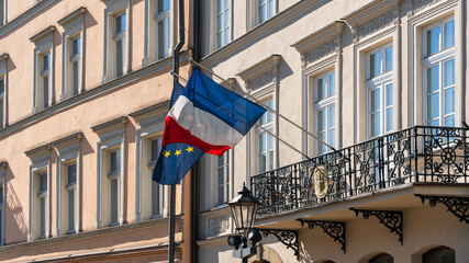 The flags of France and the European Union flutter in the wind on the old wall of the French consulate in a European city on a sunny day