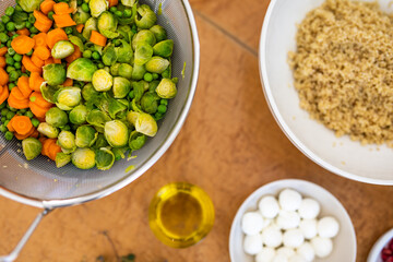 Salad preparation with brussels sprouts, carrots, peas, mozzarella, olive oil and quinoa on the kitchen table