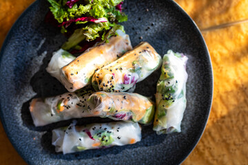 Homemade rice paper springrolls on plate with side salad in the sun on the kitchen table