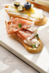 Italian antipasto bruschetta - white bread slices with smoked ham, goat cheese, blueberries, mozzarella, tomatoes, basil on marble board, glass with lemon water