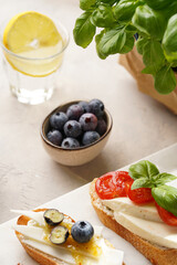 Italian antipasto bruschetta - white bread slices with smoked ham, goat cheese, blueberries, mozzarella, tomatoes, basil on marble board, glass with lemon water
