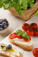 Italian antipasto bruschetta - white bread slices with smoked ham, goat cheese, blueberries, mozzarella, tomatoes, basil on marble board, glass with lemon water