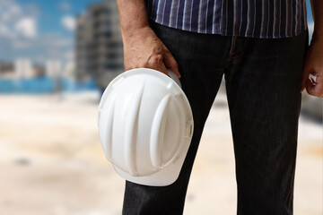 Man holding white hardhat - safety equipment. Construction in the background