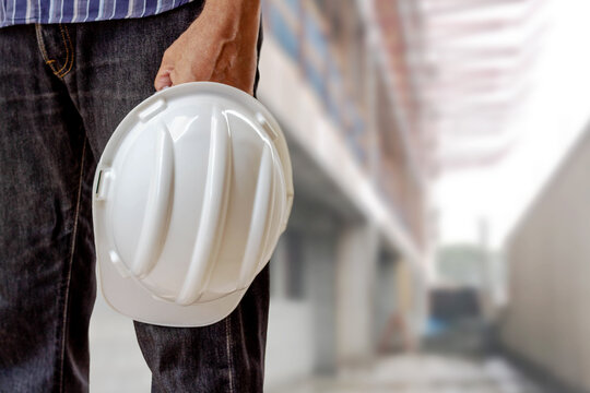 Man holding white hardhat - safety equipment. Construction in the background