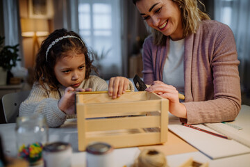 Happy little girl renovating a wooden crate together with her mother at home.