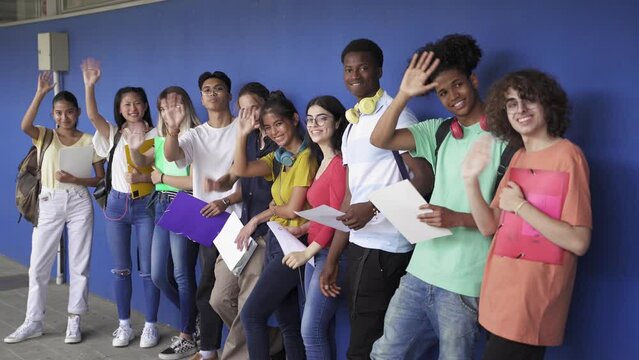 Group Of Multi Ethnic Teenager Student Friends Greeting Saying Hello To Camera Standing Over Blue Wall In The High School. Diversity In Education And Society