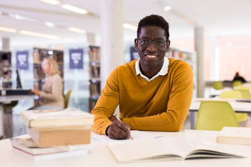 Fototapeta premium Portrait of happy african-american male student working with book in public library. High quality photo