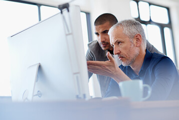 Giving some experienced advice. Shot of two colleagues having a discussion at a computer in the...