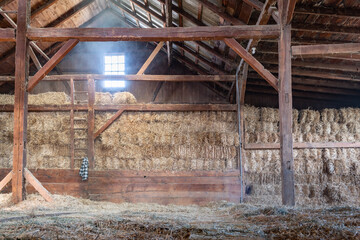 Inside of Old Worn-Down Barn With Stacked Hay Bales Dark Wooden Beams and Light Shining Through...