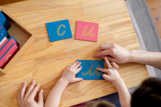 Montessori material. Mom helps her daughter learn letters using the rough alphabet.