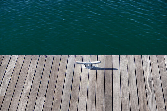 Wooden dock with mooring cleat, rippling blue-green waves in background, serenity, relaxation, vacation concept.