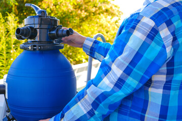 Naklejka premium Swimming pool Filter.Swimming pool cleaning equipment. water filter in the hands of a man in a blue plaid shirt on a blue pool background. A man moves the hoses to the filter in the pool.