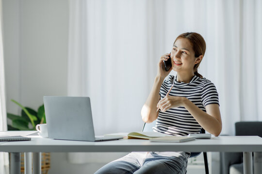 Image of young pleased happy cheerful cute beautiful Asian business woman sit indoors using laptop computer smart female working at home,E learning working at home concept