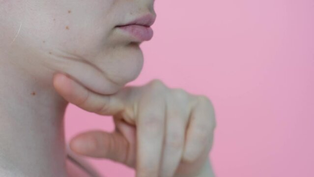 Female face with double chin close-up on pink background, side view.