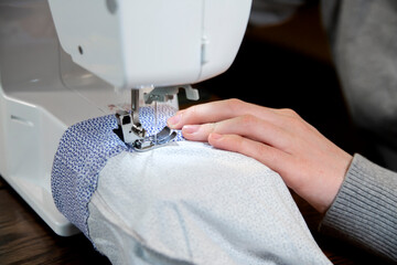 The girl sews while sitting at the sewing machine. Skill, hobby, profession.