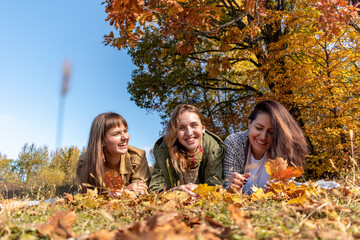 Three diverse female friends lie on the ground in the autumn forest.