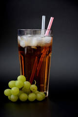 A tall glass of grape juice with ice and straws on a black background.