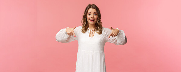 Portrait of enthusiastic upbeat young blond woman pointing fingers down to invite you check-out...