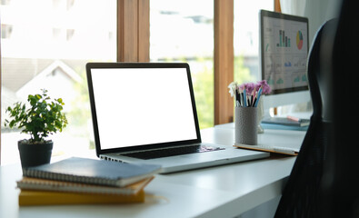 Computer laptop with empty screen, notebook and potted plant on white office desk.