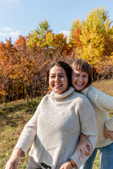 Two diverse female friends are chatting and hugging while standing in autumn forest.