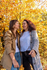 Fototapeta premium Two diverse female friends are chatting and hugging while standing in autumn forest.