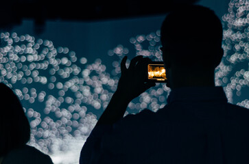 Silhouette of man taking a photo of an artistic light exhibit with a smartphone, background...
